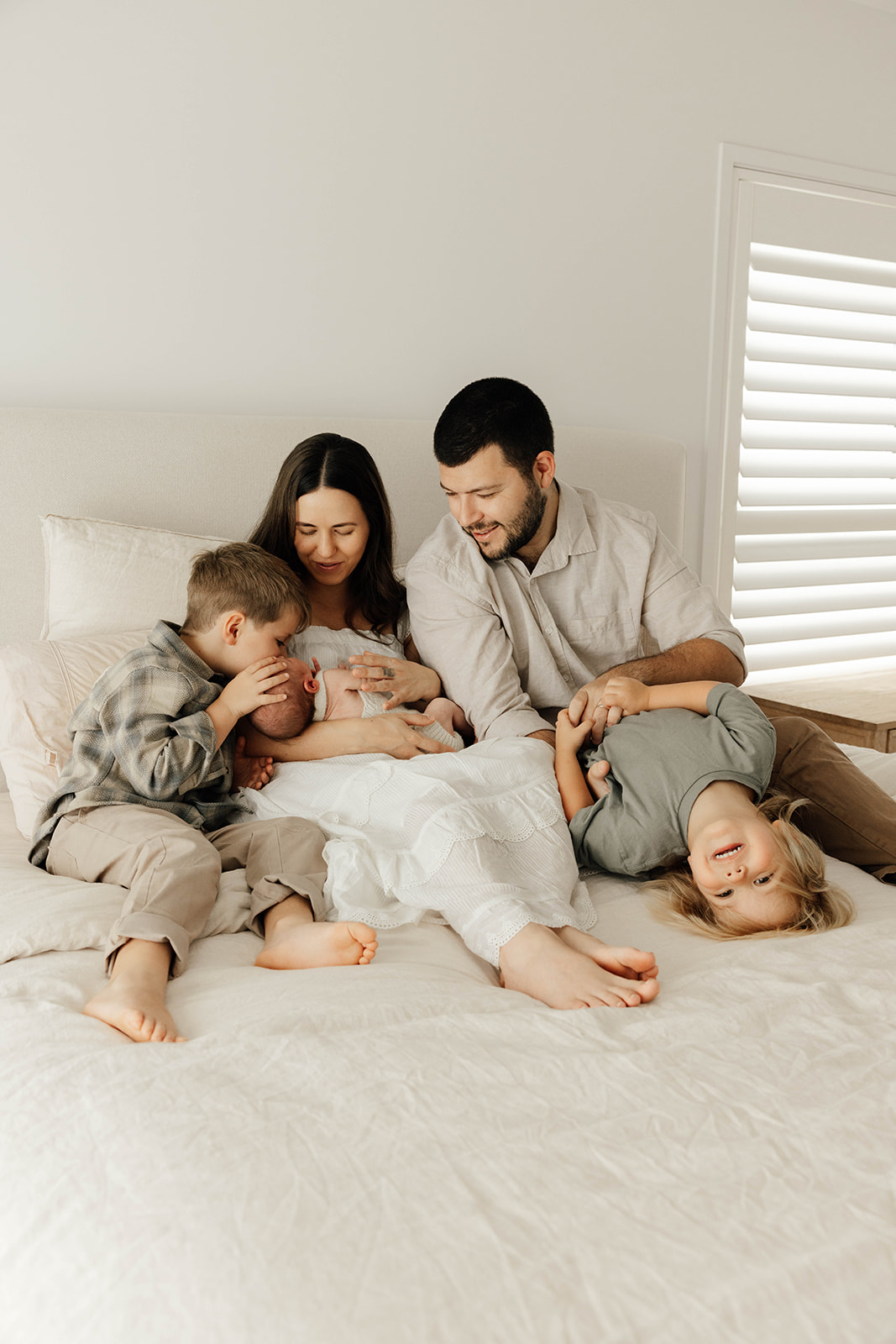 family of 5 sat on the bed looking at the newborn baby
