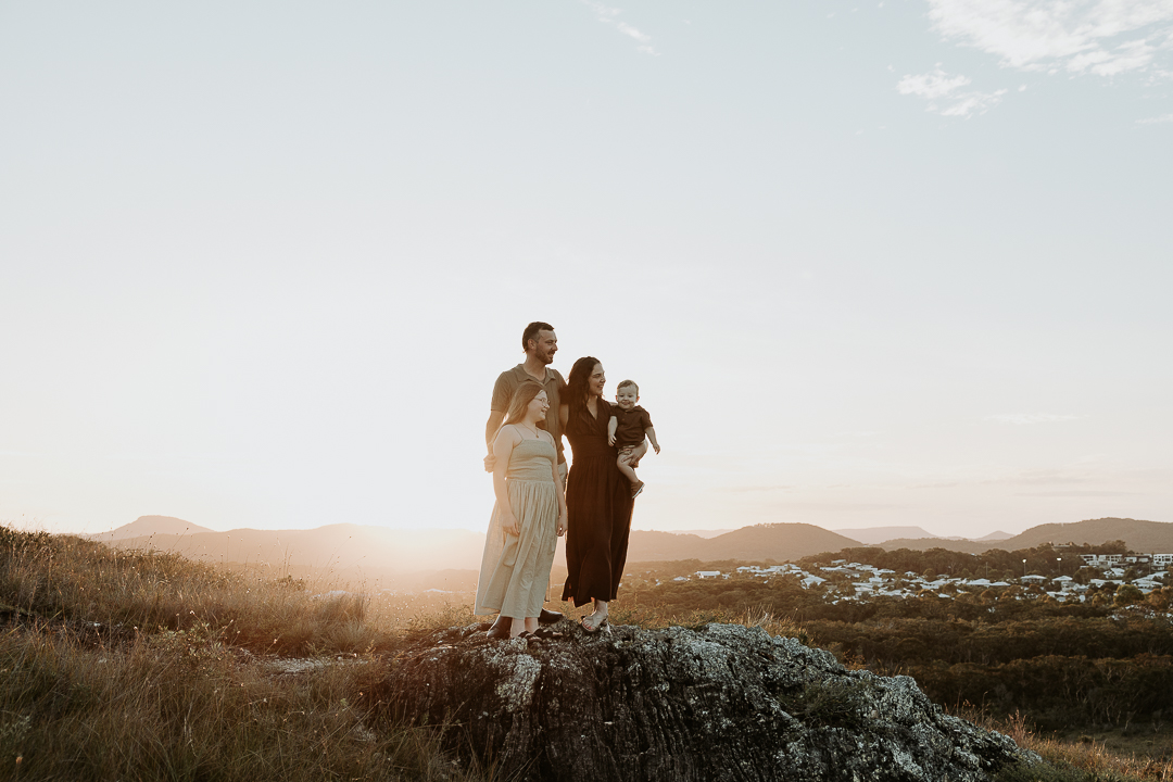 family stood together at top of mountain with the sun setting behind them