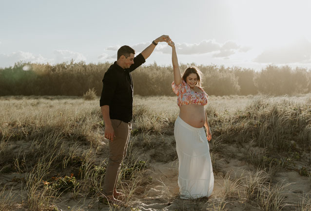 pregnant woman and her husband dancing at the beach